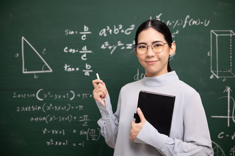 Young asian teacher woman teaching holding book and chalk video conference with student looking camera. Female teacher training the mathematics in classroom blackboard from online course.